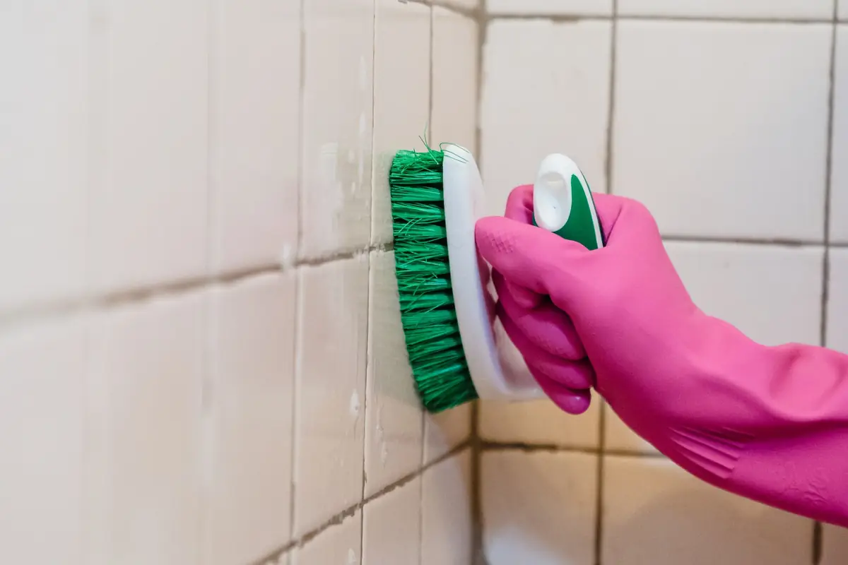 Gloved hand scrubbing tile grout with a brush during a deep cleaning