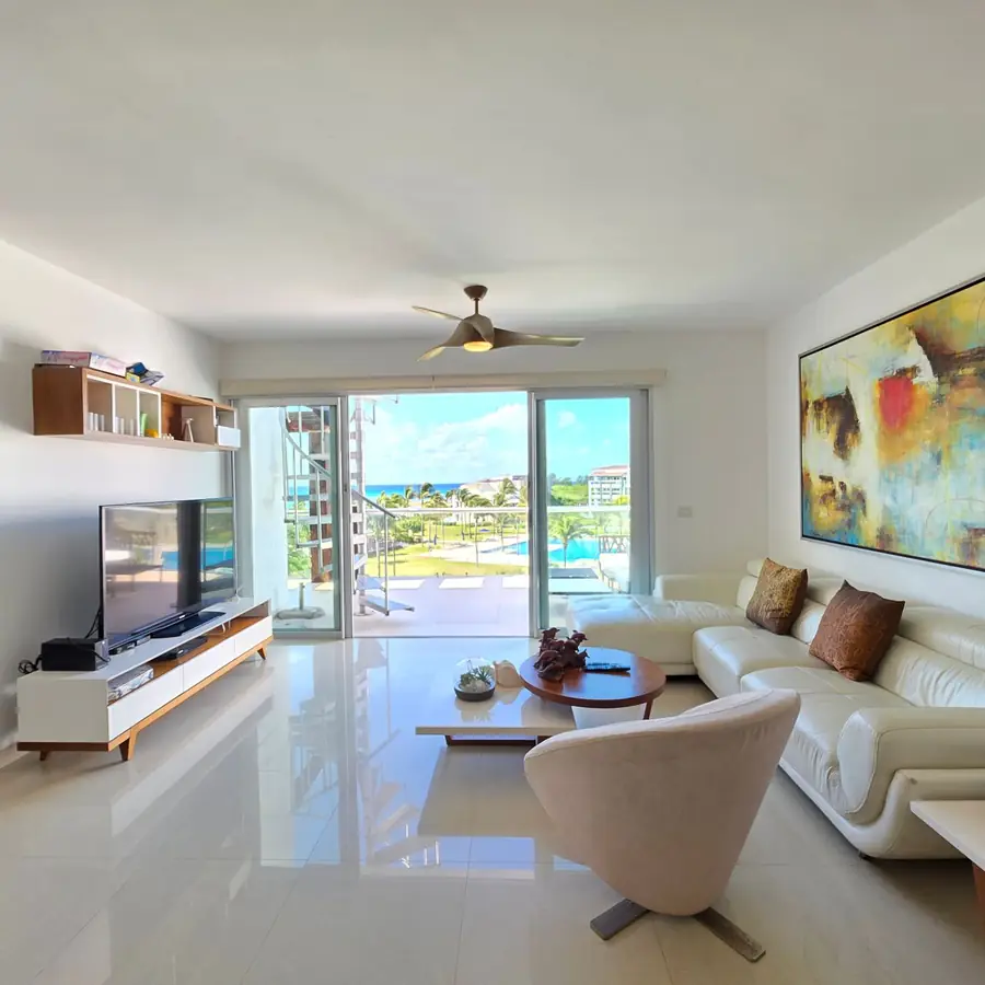 Clean, bright Florida condo living room with tile floors, a ceiling fan and a balcony view of palm trees, a pool and the ocean